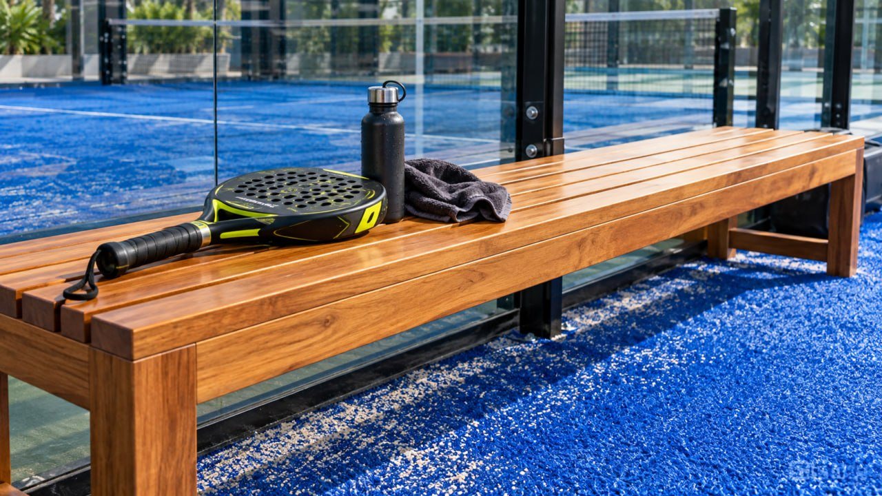 Lantai Kayu Lapangan Padel: Aturan FIP, Area yang Tepat, dan Harga 2026 5 Bangku kayu jati di sisi lapangan padel dengan raket dan botol minum